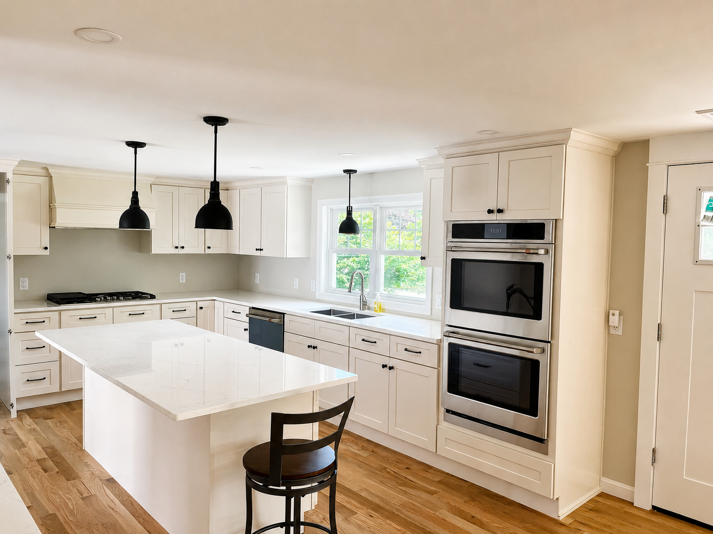 Cream shaker kitchen with quartz island, black pendant lighting and double wall ovens by Design West