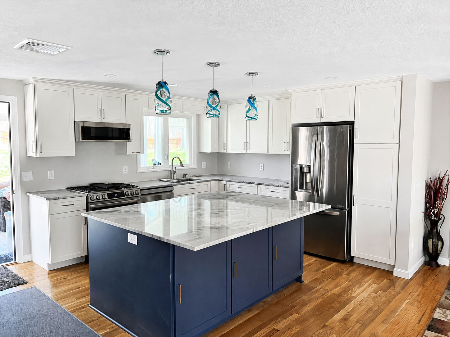 Bright kitchen with white shaker cabinetry, navy island and marble countertops by Design West